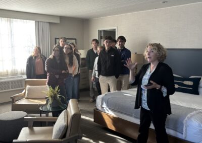 Several ILMHS students standing in a large hotel room listening to a woman speaking