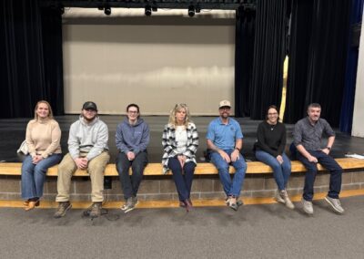 Seven adults seated on the edge of a stage